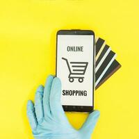 Close-up of hands in medical gloves with a smartphone. Online shopping, online banking, online payment. Payment with plastic cards. Flat Lay on a yellow background. photo