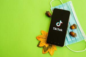 Tver, Russia - September 19, 2020. Tiktok app on the smartphone screen and medical protective mask on a green background. TikTok is a popular video sharing social network owned by ByteDance. photo