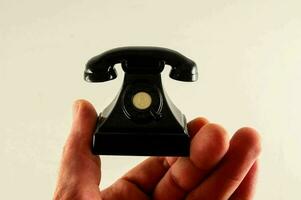 a hand holding a small black telephone in front of a white background photo