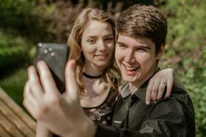 guy with a girlfriend makes a selfie in nature. young man with beautiful girl is looking at the screen of black phone. photo