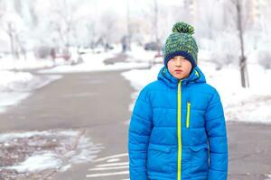 An 8-year-old boy in a blue jacket on the background of a city park after snowfall photo