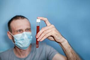 man in protective mask holds test tube with blood. Blood test for coronavirus. Develop vaccine virus. photo