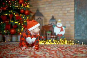 Little surprised child in santa costume in festive room on Christmas eve. Girl on background of Christmas tree. photo