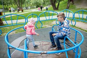 hermano y hermana paseo un carrusel en el patio de recreo en el ciudad parque. niños tener divertido en el verano al aire libre. familia en un caminar jugando juntos foto