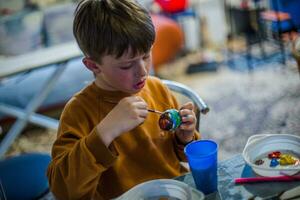 A child decorates an Easter egg in the colors of the rainbow. A child holds an egg and paints it with a brush. Preparing for the celebration of Easter. photo