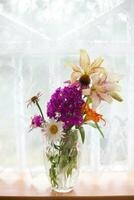 Bouquet of summer flowers in a vase standing on a sill near the window photo