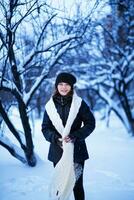 A young girl in a long white scarf on a background of snow-covered branches of trees in the city. photo