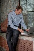 A man sits on a windowsill and works on a laptop. Beautiful man's wrist. photo