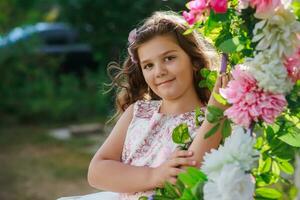 un pequeño niña en un rosado vestir en pie en frente de un floral guirnalda foto