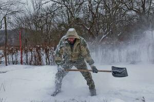 man clears the yard of snow With Shovel. Heavy snowfall in winter. High level of snow. Snowy snowdrift. photo