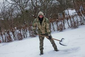 man clears the yard of snow With Shovel. Heavy snowfall in winter. High level of snow. Snowy snowdrift. photo