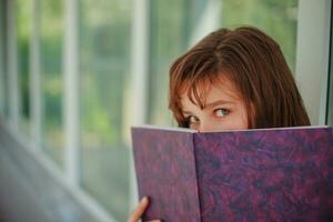 Girl schoolgirl covered her face with book. The child looks out from behind a large purple notebook. photo