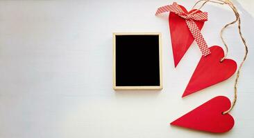 Three red wooden hearts around around wooden frame with black background. top view with copy space photo