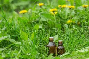 farmacéutico botella de medicina en césped en contra antecedentes de floreciente amarillo flor taraxacum oficial, o diente de león . preparación de medicinal plantas. Listo poción de césped. foto