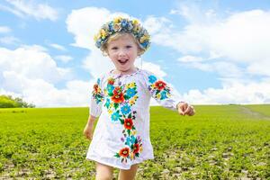 flag of Ukraine is on the shoulders of a little Ukrainian girl. Happy Ukrainian child in free Ukraine without war runs along a rural road in a field of farm soybean. International Mother Language Day. photo