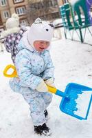 pequeño niña con grande pala alojamiento nieve en el yarda en patio de juegos. activo juegos fuera de casa en invierno durante nevada foto