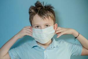 boy wears protective medical mask on face. child tucks the gum behind ears from mask. child with flu, influenza or cold protected from viruses among patients with coronavirus photo
