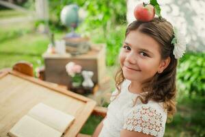 beautiful girl at desk with red apple on head. Learning outside the auditorium during coronavirus quarantine. Back to school concept. photo