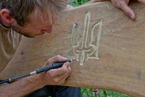 Woodwork. man cuts out the coat of arms of Ukraine on the bench. photo