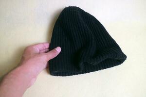 A hand holding a Black beanie, made from knitted fabric. on a white or cream background photo