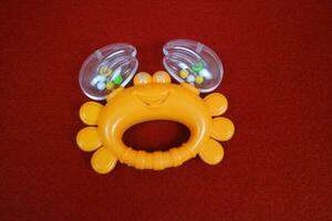 Yellow crab shaped children's toy, with small balls inside, makes a loud sound. On red background photo