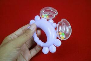 A hand holding Purple crab shaped children's toy, with small balls inside, makes a loud sound. On red background photo