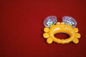 Yellow crab shaped children's toy, with small balls inside, makes a loud sound. On red background photo