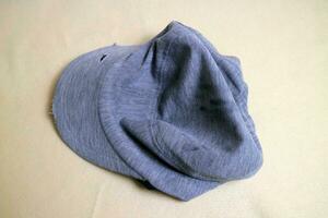 The gray cloth hat is in a worn condition with several tears. Cream background photo
