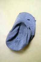 The gray cloth hat is in a worn condition with several tears. Cream background photo