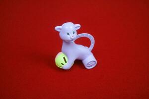 A toy shaped like an alpaca animal, purple color, holding a ball. on a red background photo