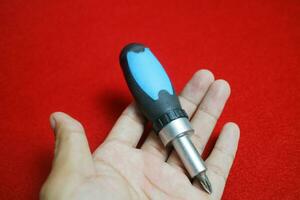 A hand holding a Mini stainless steel screwdriver with black and blue handle, on a red background photo