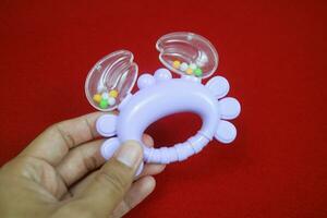 A hand holding Purple crab shaped children's toy, with small balls inside, makes a loud sound. On red background photo