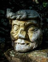 a stone head with a face on it in the woods photo