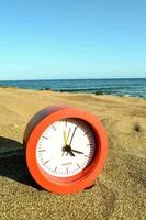 a red alarm clock on the beach with the ocean in the background photo