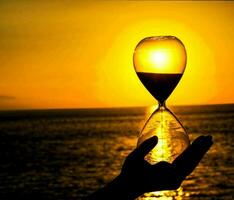 a person holding an hourglass in front of the sun photo