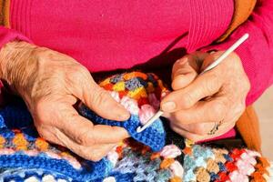 an older woman is knitting a colorful crochet blanket photo