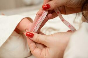 mother measures the size of a newborn baby's feets, close-up photo