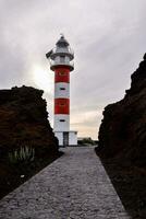 a red and white lighthouse stands in the middle of a rocky area photo