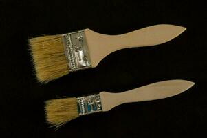 two paint brushes with wooden handles on a black background photo