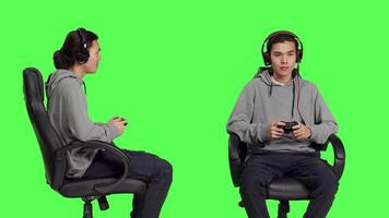 Skilled man playing online videogames in studio, having fun with people on gaming multiplayer challenge over greenscreen backdrop. Asian guy enjoying competition with gamers. video