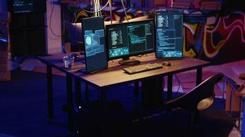 Jib down shot of advanced technology computer system running malicious code in empty warehouse. PC monitors in empty graffiti painted underground hideout used by hackers to commit illicit activities video