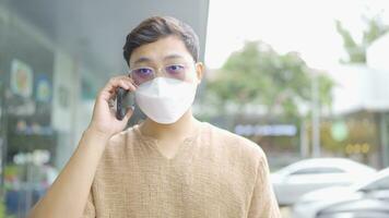 A man wearing a protective face mask walks and talks on the phone in a building. video