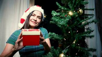 vrouw in de kerstman claus hoed staat nieuw jaar geschenk in een karton doos Aan Kerstmis voor de familie, vrouw, nieuw jaar vakantie. video