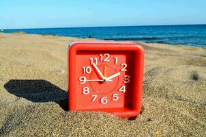 a red clock sitting in the sand on the beach photo