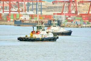 two tug boats in the water near a large container ship photo