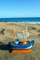 a toy boat on the beach near the ocean photo