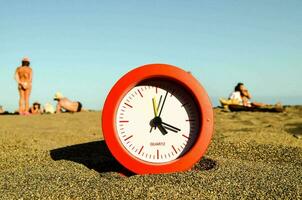 a red clock sitting in the sand on a beach photo