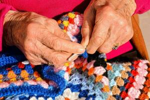 an elderly woman is knitting a colorful crochet blanket photo