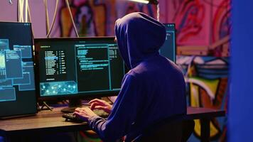 Hacker in graffiti painted hideaway base writing lines of code on computer, developing malware that get past security systems. Rogue programmer uses PC in bunker, running hacking script video