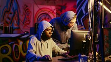 New member in hacking group receiving guidance from knowledgeable rogue programmer acting as his mentor in hidden base. African american hacker teaches script kiddie how to hack computers video